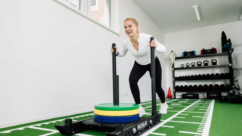 Frau führt Krafttraining mit Gewichtsschlitten auf Kunstrasen in der Physiotherapie-Praxis durch.