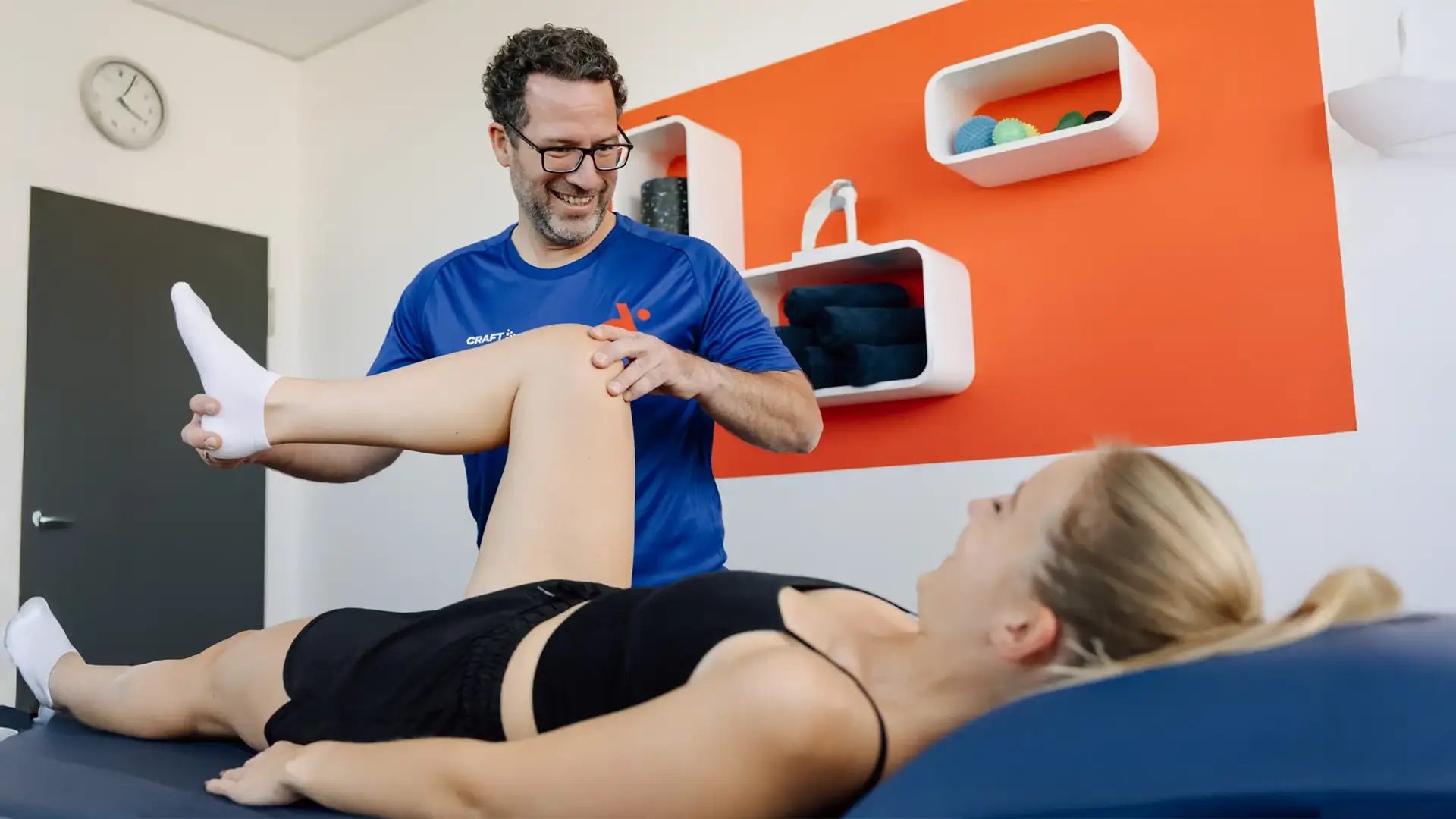 Physiotherapeut mobilisiert das Bein einer liegenden Patientin auf der Behandlungsliege.