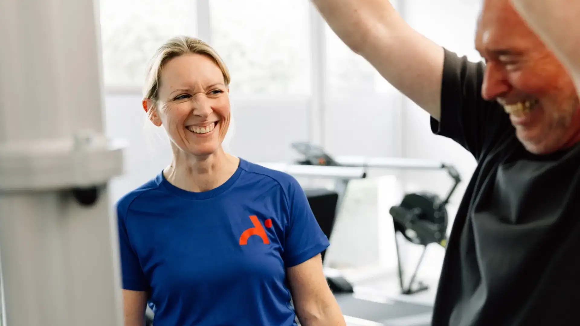 Physiotherapeutin lacht mit Patient während einer Trainingssitzung im Gerätebereich.