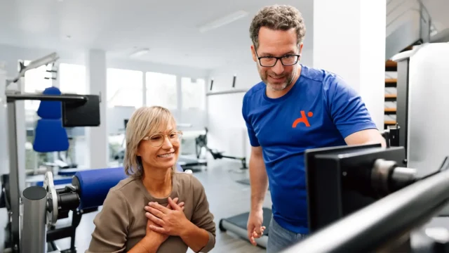 Physiotherapeut berät Patientin am Trainingsgerät und erklärt die digitale Auswertung.