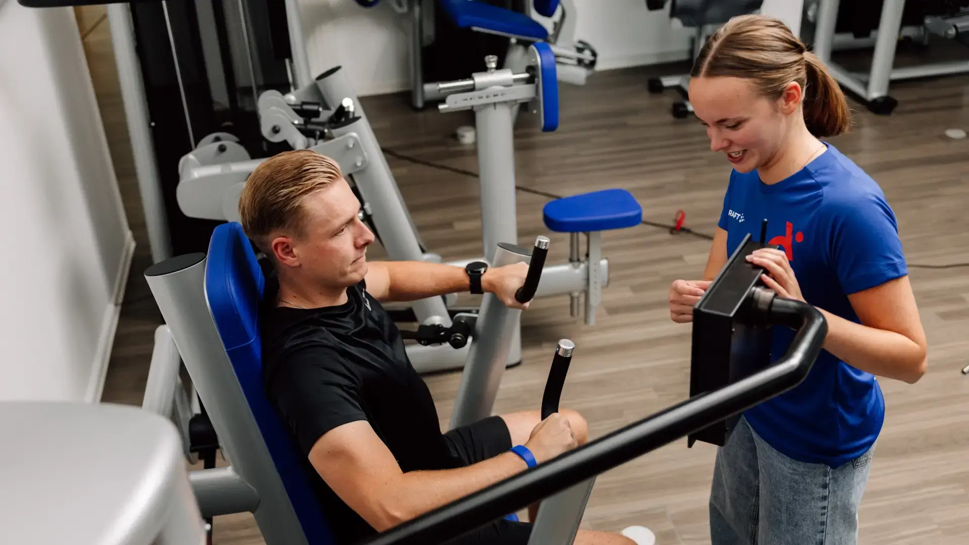 Physiotherapeutin erklärt die Geräteeinstellungen während des Trainings an der Brustpresse.