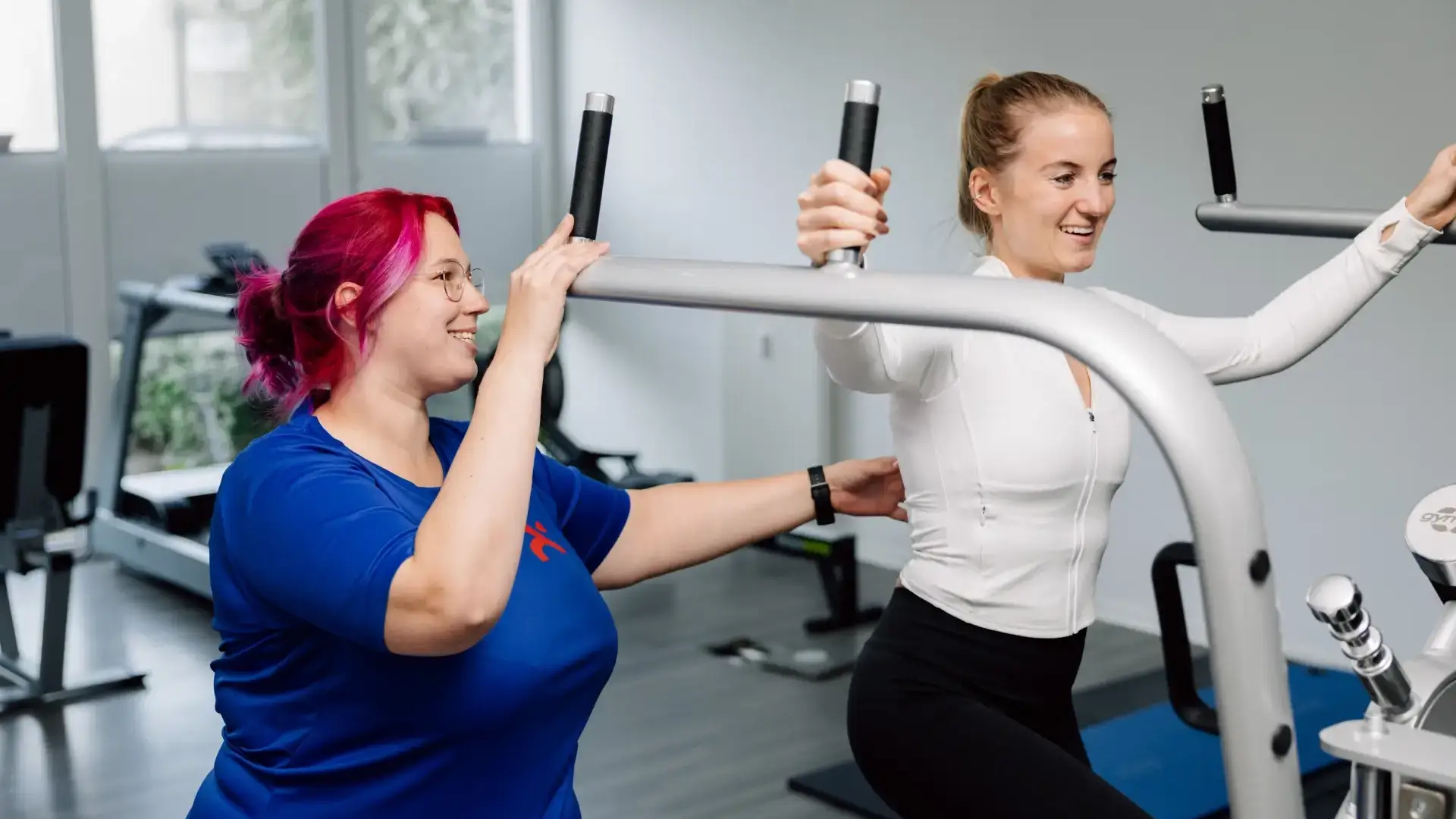 Physiotherapeutin unterstützt Patientin bei einer Schulterübung im Trainingsraum.