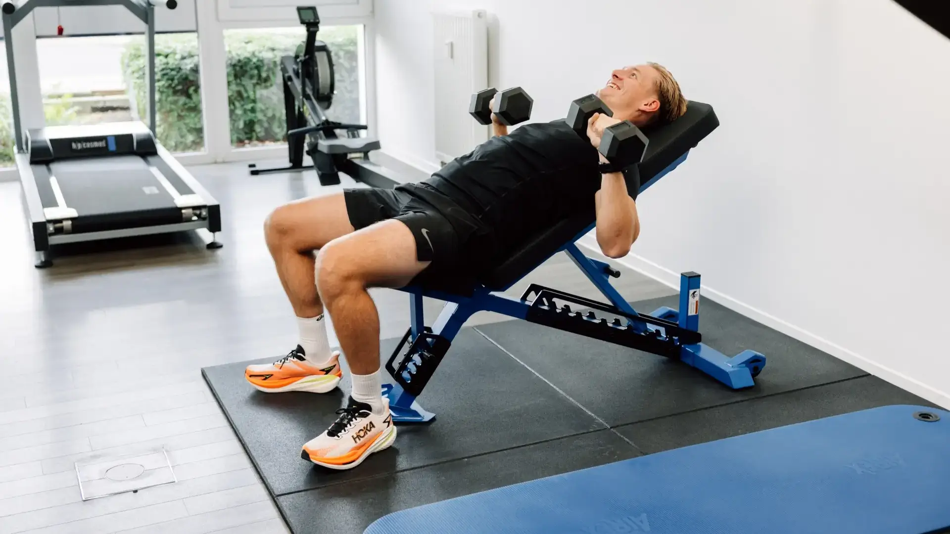 Patient führt Bankdrücken mit Kurzhanteln im Trainingsraum der Physiotherapie Ambrassat durch.