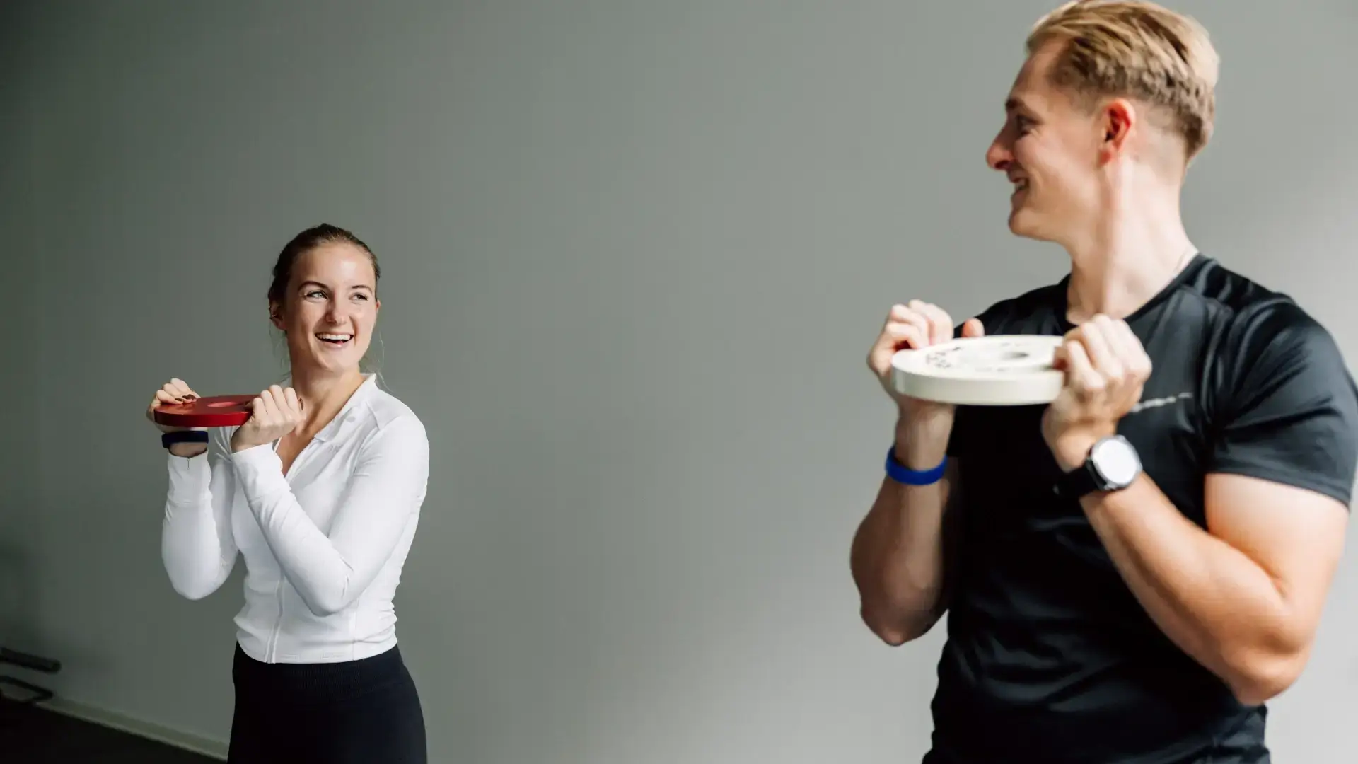 Zwei Personen trainieren gemeinsam mit Gewichtsscheiben und lachen während der Übung.