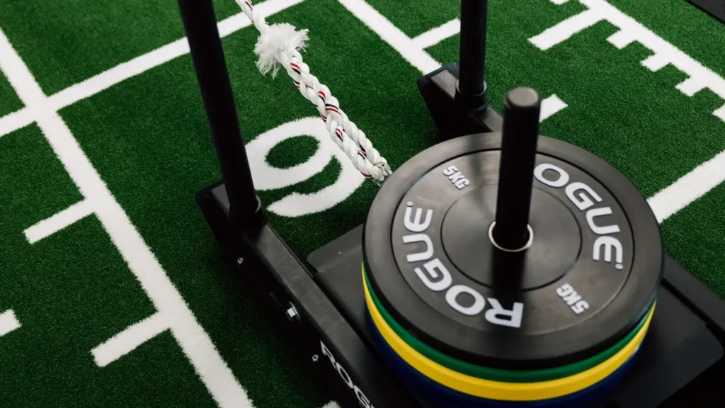 Detailaufnahme eines Gewichtsschlittens mit Hantelscheiben auf grünem Kunstrasen.