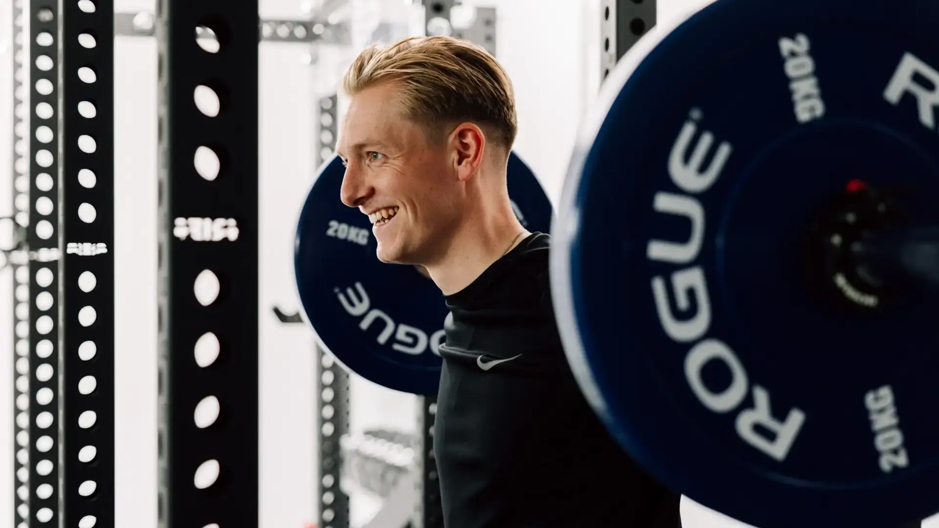 Mann trainiert an der Langhantelstation mit blauen Gewichtsscheiben im Trainingsraum.