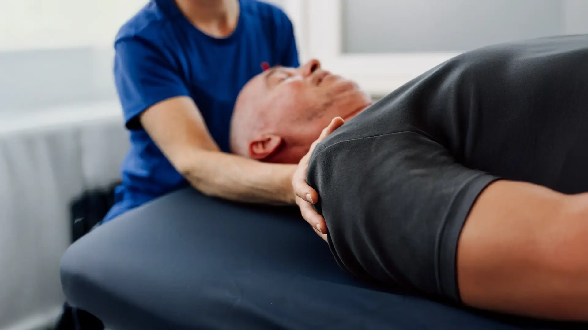 Manuelle Therapie am Kiefer- und Schulterbereich eines Patienten, Fokus auf Entspannung und Mobilisation der Muskulatur.